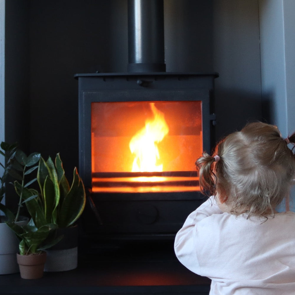 A dog sitting next to an alight log burner