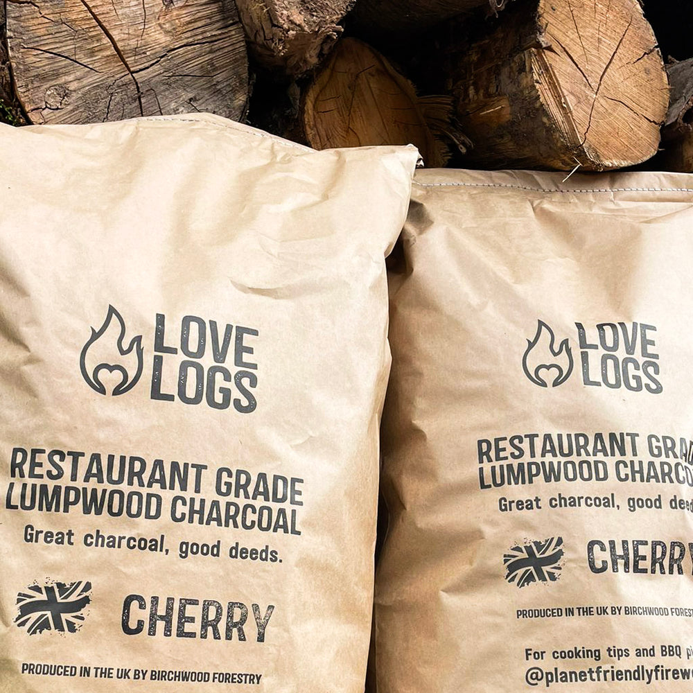 Love Logs Wild Cherry British Charcoal in front of cherry wood pile