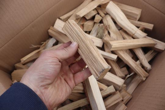 
                      
                        A box of pizza oven oak kindling with a hand holding one piece up
                      
                    